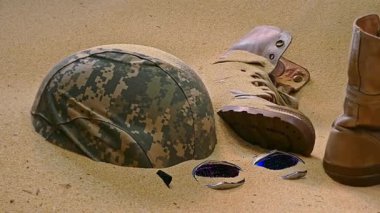 Terk edilmiş askeri teçhizat, yıpranmış bir bot, kask ve parçalanmış koruyucu gözlük, kısmen çöl kumuna gömülmüş, çatışmanın acı gerçeklerini simgeliyor..