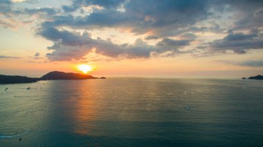 Gün batımında bir kıyı koyunun nefes kesici hava manzarası, sakin denizi ve uzaktaki siluetli tepeleri yansıtan altın ışık. Patong Körfezi Phuke 'deki altın güneşin güzel yansıması.
