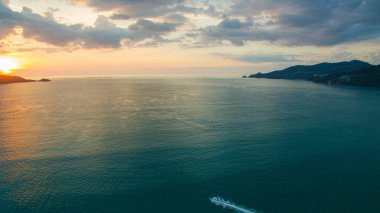 Gün batımında bir kıyı koyunun nefes kesici hava manzarası, sakin denizi ve uzaktaki siluetli tepeleri yansıtan altın ışık. Patong Körfezi Phuke 'deki altın güneşin güzel yansıması.