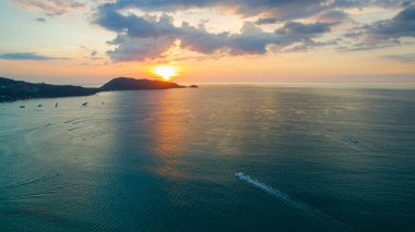 Gün batımında bir kıyı koyunun nefes kesici hava manzarası, sakin denizi ve uzaktaki siluetli tepeleri yansıtan altın ışık. Patong Körfezi Phuke 'deki altın güneşin güzel yansıması.