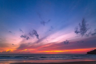 Alacakaranlıkta sakin bir sahil sahnesi, canlı bir günbatımı sergiliyor sakin sulara ve ıslak kuma yansıyan renkli bulutlarla. Karon plajında gün batımında muhteşem bir gökyüzü. Tatlı gökyüzü