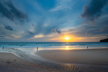 Alacakaranlıkta sakin bir sahil sahnesi, canlı bir günbatımı sergiliyor sakin sulara ve ıslak kuma yansıyan renkli bulutlarla. Karon plajında gün batımında muhteşem bir gökyüzü. tatlı gökyüzü arkaplanı