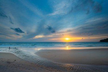 Alacakaranlıkta sakin bir sahil sahnesi, canlı bir günbatımı sergiliyor sakin sulara ve ıslak kuma yansıyan renkli bulutlarla. Karon plajında gün batımında muhteşem bir gökyüzü. tatlı gökyüzü arkaplanı