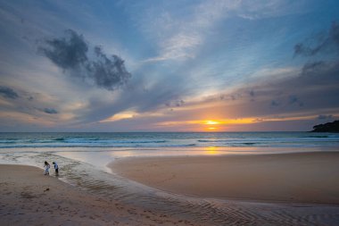 Alacakaranlıkta sakin bir sahil sahnesi, canlı bir günbatımı sergiliyor sakin sulara ve ıslak kuma yansıyan renkli bulutlarla. Karon plajında gün batımında muhteşem bir gökyüzü. tatlı gökyüzü arkaplanı