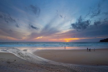 Alacakaranlıkta sakin bir sahil sahnesi, canlı bir günbatımı sergiliyor sakin sulara ve ıslak kuma yansıyan renkli bulutlarla. Karon plajında gün batımında muhteşem bir gökyüzü. tatlı gökyüzü arkaplanı