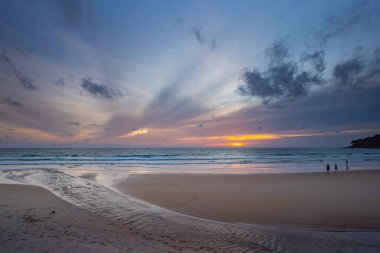 Alacakaranlıkta sakin bir sahil sahnesi, canlı bir günbatımı sergiliyor sakin sulara ve ıslak kuma yansıyan renkli bulutlarla. Karon plajında gün batımında muhteşem bir gökyüzü. tatlı gökyüzü arkaplanı