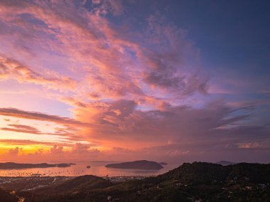 Canlı bir gün doğumunun nefes kesici panoramik görüntüsü kıyı kasabasının üzerine sıcak renkler döküyor, deniz gökyüzünün ve tepelerin ateşli renklerini yansıtıyor ve sakin manzarayı çerçeveliyor..