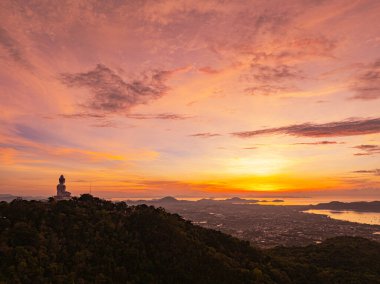 Phuket 'in tepesindeki Arial manzarası. Dağdaki büyük Buda. Canlı bir gün doğumunun nefes kesici panoramik görüntüsü. Sahil kasabasının üzerine ılık renkler döküyor. Gökyüzünü yansıtan deniz.