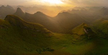 Yükselen dağlarla çevrili yemyeşil bir vadinin nefes kesici hava manzarası. Dolambaçlı bir nehir, berrak ve geniş bir gökyüzünün altında doğal bir güzellik hissi yaratarak, huzurlu bir manzarayı keser.