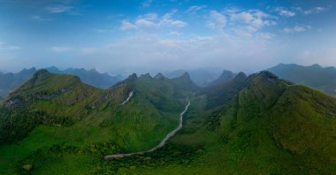 Yükselen dağlarla çevrili yemyeşil bir vadinin nefes kesici hava manzarası. Dolambaçlı bir nehir, berrak ve geniş bir gökyüzünün altında doğal bir güzellik hissi yaratarak, huzurlu bir manzarayı keser.