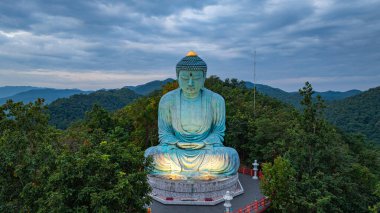 Bereketli ormanlarla çevrili, dingin bir Buda heykeli. Arka planda, sisli bir dağ manzarasının üzerine canlı renkler saçan çarpıcı bir gündoğumu. Gün doğumunda güzel gökyüzü. 