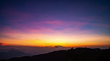 Güneş sık bir ormanın arkasında batıyor, dalgalı bulutlar ve sislerin arasından altın bir parıltı saçıyor. Bu büyüleyici sahne sıcak ve serin tonlarla harmanlanarak dramatik ve sakin bir doğal manzara yaratır..