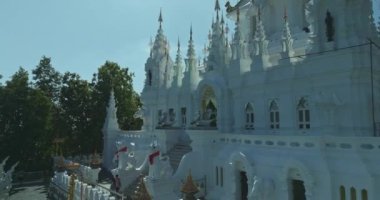 Bereketli yeşil bir tepenin üzerinde, açık mavi gökyüzünün altında canlı orman dağlarıyla çevrili süslü beyaz bir tapınak. Karmaşık bir mimari ve dingin bir güzellik sergiliyor..