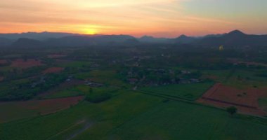 Parlak günbatımı gökyüzünün altında uzun, renkli bir dağ sırasının ve bir ayçiçeği tarlasının güzel manzarası. Bu görüntü, kırsal kesimin doğal güzelliğini, sükunetini ve çekiciliğini yansıtıyor..