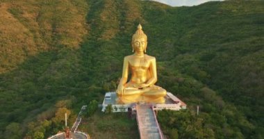 Gün batımının canlı renkleri sırasında yakalanan dingin bir vadiye bakan bir tepenin tepesindeki büyük altın Buda heykelinin hayranlık uyandırıcı görüntüsü. Lopburi Tayland 'daki en büyük altın Buda' nın hava manzarası.