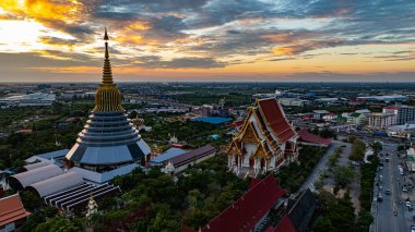 Hava Wat Ketmadi Sriwararam perspektifi bulutlu mavi gökyüzü altında şehir ve kırsal alanlarla çevrili büyüleyici bir Tayland tapınak kompleksi sergiliyor..