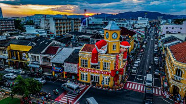 Phuket, Tayland-Aralık, 25. 2024: Phuket Eski Şehir saat kulesinin hareketli bir görüntüsü Noel Baba süslemeleri ile süslenmiş, hareketli sokaklar ve günbatımında canlı mimari ile çevrili.