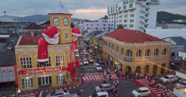 Phuket, Tayland-Aralık, 25. 2024: Büyük Noel Baba ve Noel Anne süslemeleriyle süslenmiş tarihi sarı saat kulesinin olduğu canlı bir sahne dramatik bir akşam gökyüzü. Mutlu yıllar 2024