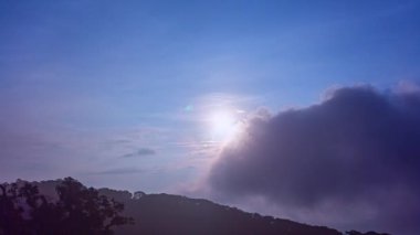 Yoğun bir ormanın üzerinde zaman aşımına uğrayan gün doğumu, dalgalı bulutlar ve sislerin arasından altın bir parıltı saçıyor. Bu büyüleyici sahne sıcak ve serin tonlarla harmanlanarak dramatik ve sakin bir doğal manzara yaratır..