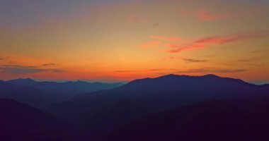Güneşin doğuşunda bulutları mavi gökyüzüne doğru aydınlatan parlak turuncu ve pembe renkler ile çarpıcı bir dağ manzarası. Sis tabakası vadiye yerleşmiş, manzaraya rüya gibi bir manzara katmış..