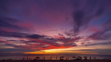 Okyanusun üzerinde canlı bir günbatımının yer aldığı çarpıcı sahil manzarası. Dinamik gökyüzü turuncu, pembe ve mor renklerle boyanarak sakin ve resimli bir kıyı sahnesi oluşturur..