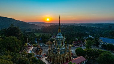 Gün doğumuyla birlikte Chiang Mai 'deki Mae Klang Şelalesi Tapınağı' nın hava görüntüsü sakin gökyüzünde sıcak renkler bırakıyor. Huzurlu ortam, tapınağın ve doğal manzaranın dingin güzelliğini vurguluyor..