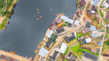 Göl kenarındaki bir köyün havadan görünüşü, kırsal mimari, yemyeşil ve sakin sulara dağılmış teknelerin karışımı sergileniyor. Doğal güzellik ve insan yerleşiminin ahenkli bir karışımı.
