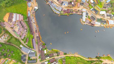 Göl kenarındaki bir köyün havadan görünüşü, kırsal mimari, yemyeşil ve sakin sulara dağılmış teknelerin karışımı sergileniyor. Doğal güzellik ve insan yerleşiminin ahenkli bir karışımı.