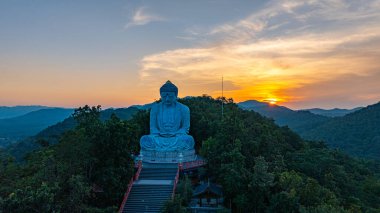 Bereketli ormanlarla çevrili, dingin bir Buda heykeli. Arka planda, sisli bir dağ manzarasının üzerine canlı renkler saçan çarpıcı bir gündoğumu. Gün doğumunda güzel gökyüzü. 
