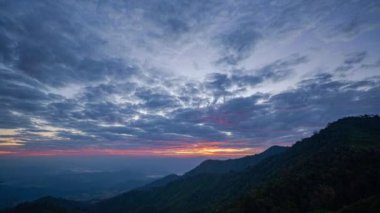 Gökyüzünde turuncu, pembe ve mavi renklerin pürüzsüz bir şekilde harmanlandığı katmanlanmış dağ siluetlerinin üzerindeki renkli günbatımının nefes kesen görüntüsü. Zirveden gelen ışık huzmeleri