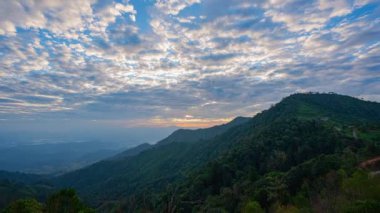 Gökyüzünde turuncu, pembe ve mavi renklerin pürüzsüz bir şekilde harmanlandığı katmanlanmış dağ siluetlerinin üzerindeki renkli günbatımının nefes kesen görüntüsü. Zirveden gelen ışık huzmeleri