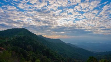 Gökyüzünde turuncu, pembe ve mavi renklerin pürüzsüz bir şekilde harmanlandığı katmanlanmış dağ siluetlerinin üzerindeki renkli günbatımının nefes kesen görüntüsü. Zirveden gelen ışık huzmeleri