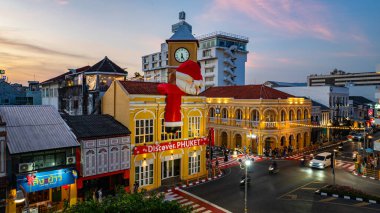 Phuket, Tayland-30 Aralık 2024 'te devasa Noel Baba ve Noel Anne süslemeleriyle süslenmiş tarihi sarı saat kulesinin olduğu canlı bir sahne. Mutlu yıllar 2025