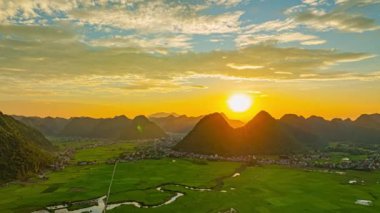 Gün batımında huzurlu bir dağ vadisinin havadan görünüşü, çarpıcı kireçtaşı tepelerinin silueti, canlı bir gökyüzüne karşı. Görüntü, doğal manzaralar ve aşağıdaki kırsal tarım arazileri arasındaki uyumu yakalar.