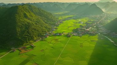 Sis kaplı Karst dağları tarafından çerçevelenmiş dolambaçlı nehir ve pirinç tarlalarıyla dolu verimli bir vadinin üzerinde huzurlu bir gün doğumu. Sahne huzur ve doğal güzellik yayar, şafağın yumuşak, sıcak ışığını yakalar.