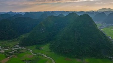 Sis kaplı Karst dağları tarafından çerçevelenmiş dolambaçlı nehir ve pirinç tarlalarıyla dolu verimli bir vadinin üzerinde huzurlu bir gün doğumu. Sahne huzur ve doğal güzellik yayar, şafağın yumuşak, sıcak ışığını yakalar.