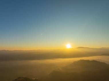 Güzel güneş, vadide sislerin üzerinde parlıyor. Sis bulutu dağın tepesini kaplıyor. Sis denizi gibi. Mükemmel ormanın üzerinde mavi gökyüzünde beyaz bulut.