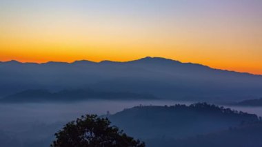 Zaman su gibi akıp geçiyor vadideki sislerin üzerinde. Ufukta güneşin parlak ışığının sebep olduğu tatlı bir gökyüzü var. Güneşin renkli gökyüzü.