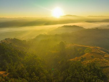 Parlak, berrak mavi gökyüzünün altındaki yemyeşil bir dağ sırasının hava manzarası. Güneş ışığı altındaki geniş, yuvarlak arazi ve vadileri aydınlatıyor..