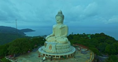 Havadan bakıldığında bulutların arasından güneş ışığı yükseliyor ve Phuket 'te parlıyor. Büyük Buda bir dağın tepesine tünemiş. Seyahat ve ibadet konsepti için 4K video. Phuket 'in ünlü simgesi.
