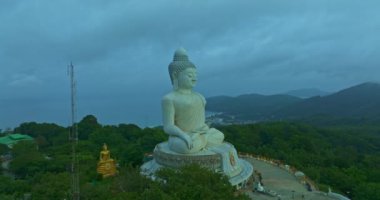 Havadan bakıldığında bulutların arasından güneş ışığı yükseliyor ve Phuket 'te parlıyor. Büyük Buda bir dağın tepesine tünemiş. Seyahat ve ibadet konsepti için 4K video. Phuket 'in ünlü simgesi.