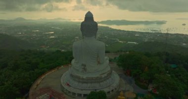 Havadan bakıldığında bulutların arasından güneş ışığı yükseliyor ve Phuket 'te parlıyor. Büyük Buda bir dağın tepesine tünemiş. Seyahat ve ibadet konsepti için 4K video. Phuket 'in ünlü simgesi.