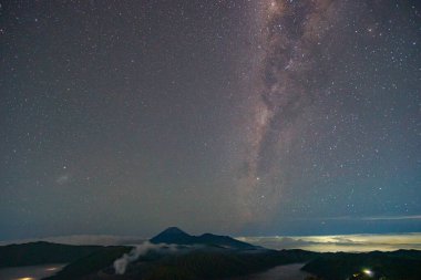 Volkan Bromo 'nun üzerindeki Samanyolu çok güzel kümelenmiş. Bulutlar takip ediyor, gökyüzünü ve yıldızları karalıyor. Gece gökyüzü yıldızlarla parıldıyor. harika ve büyüleyici bir resim..