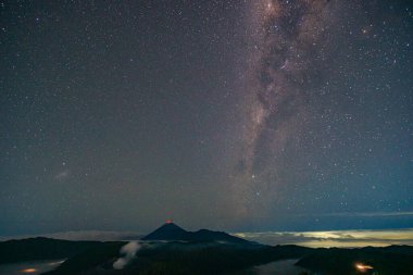 Volkan Bromo 'nun üzerindeki Samanyolu güzel bir şekilde kümelenmiş. Bulutlar takip ediyor, gökyüzünü ve yıldızları karalıyor. Gece gökyüzü yıldızlarla parıldıyor. harika ve büyüleyici bir resim..