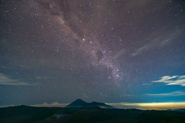 Volkan Bromo 'nun üzerindeki Samanyolu güzel bir şekilde kümelenmiş. Bulutlar takip ediyor, gökyüzünü ve yıldızları karalıyor. Gece gökyüzü yıldızlarla parıldıyor. harika ve büyüleyici bir resim..
