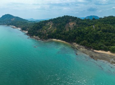 Sarmal yolları, kristal berraklığında turkuaz suları ve parçalı bulutlu bir gökyüzünün altındaki uzak adaları olan yemyeşil bir kıyı şeridinin nefes kesici hava manzarası. Lam Nga Silay Adası 'nda, Phuket. yeşil deniz