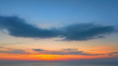 Zaman aşımı. Okyanusun üzerinde canlı bir günbatımının olduğu çarpıcı bir sahil manzarası. İnsanların siluetleri ve kumlu sahilde renkli şemsiyeler..