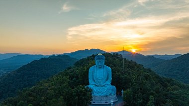 Bereketli ormanlarla çevrili, dingin bir Buda heykeli. Arka planda, sisli bir dağ manzarasının üzerine canlı renkler saçan çarpıcı bir gündoğumu. Gün doğumunda güzel gökyüzü. 