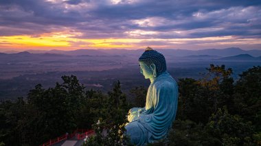 Bereketli ormanlarla çevrili, dingin bir Buda heykeli. Arka planda, sisli bir dağ manzarasının üzerine canlı renkler saçan çarpıcı bir gündoğumu. Gün doğumunda güzel gökyüzü. 