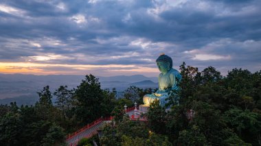 Bereketli ormanlarla çevrili, dingin bir Buda heykeli. Arka planda, sisli bir dağ manzarasının üzerine canlı renkler saçan çarpıcı bir gündoğumu. Gün doğumunda güzel gökyüzü. 